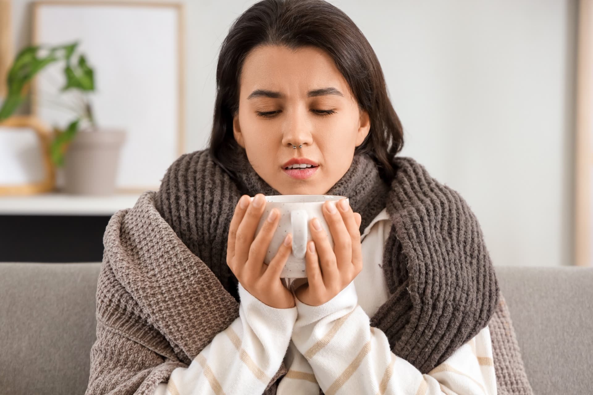 Femme enrhumée enveloppée dans un châle, tenant une tasse chaude
